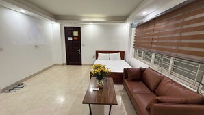 Habitación de hotel con cama, sofá de cuero marrón, mesa de madera con un florero y ventana con persianas.