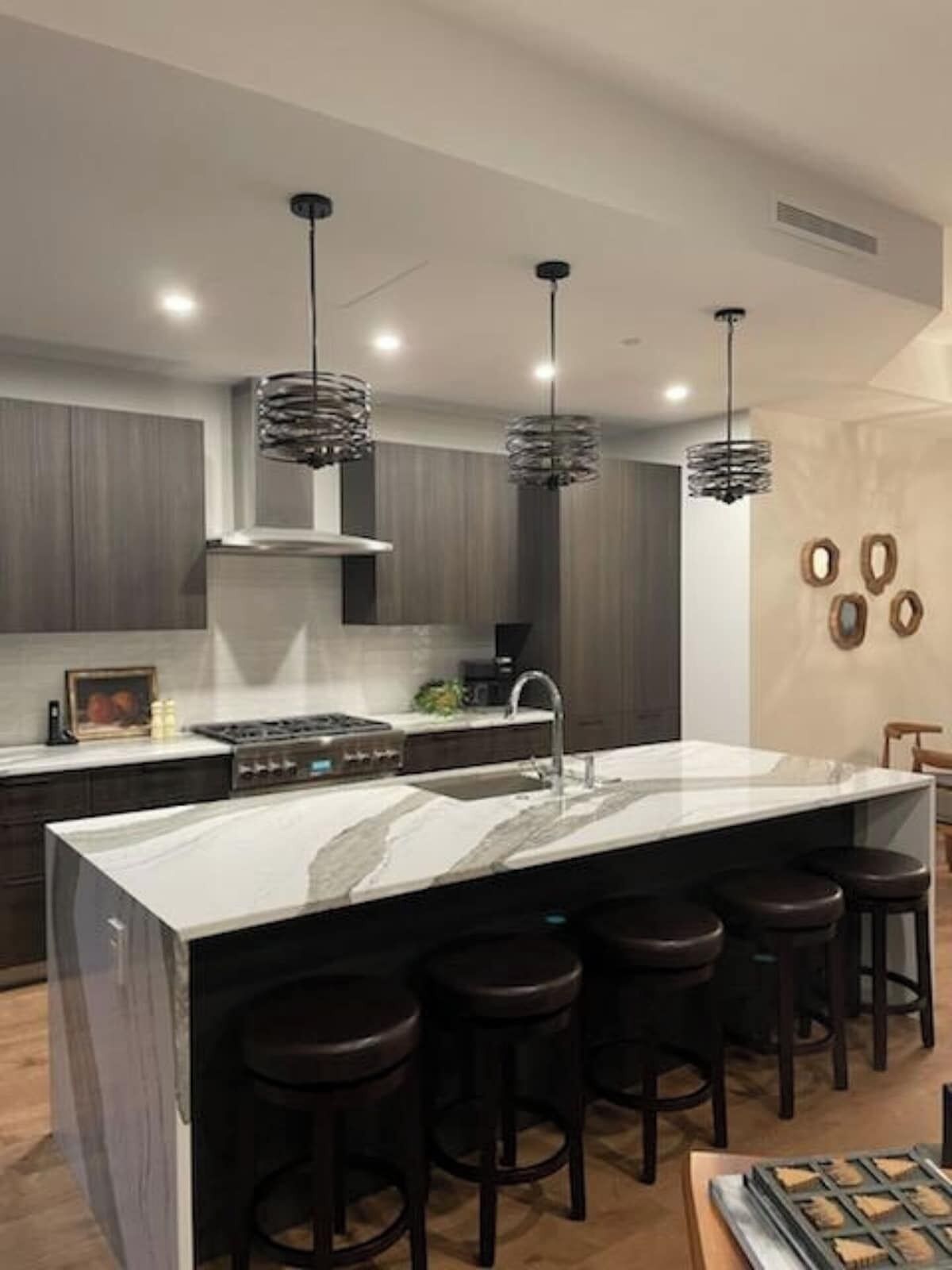 Une cuisine moderne dotée d’un grand îlot central, de tabourets de bar, de luminaires suspendus et d’une cuisinière.