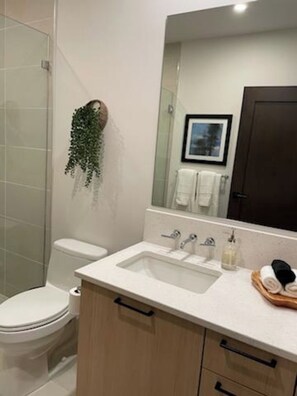 A modern bathroom with a toilet, sink, and mirror. There is a towel rack with a towel and a small plant.