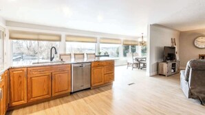 Una cocina amplia con armarios de madera, lavavajillas y una isla grande. Hay un comedor con mesa y sillas, y un sofá en la sala de estar.