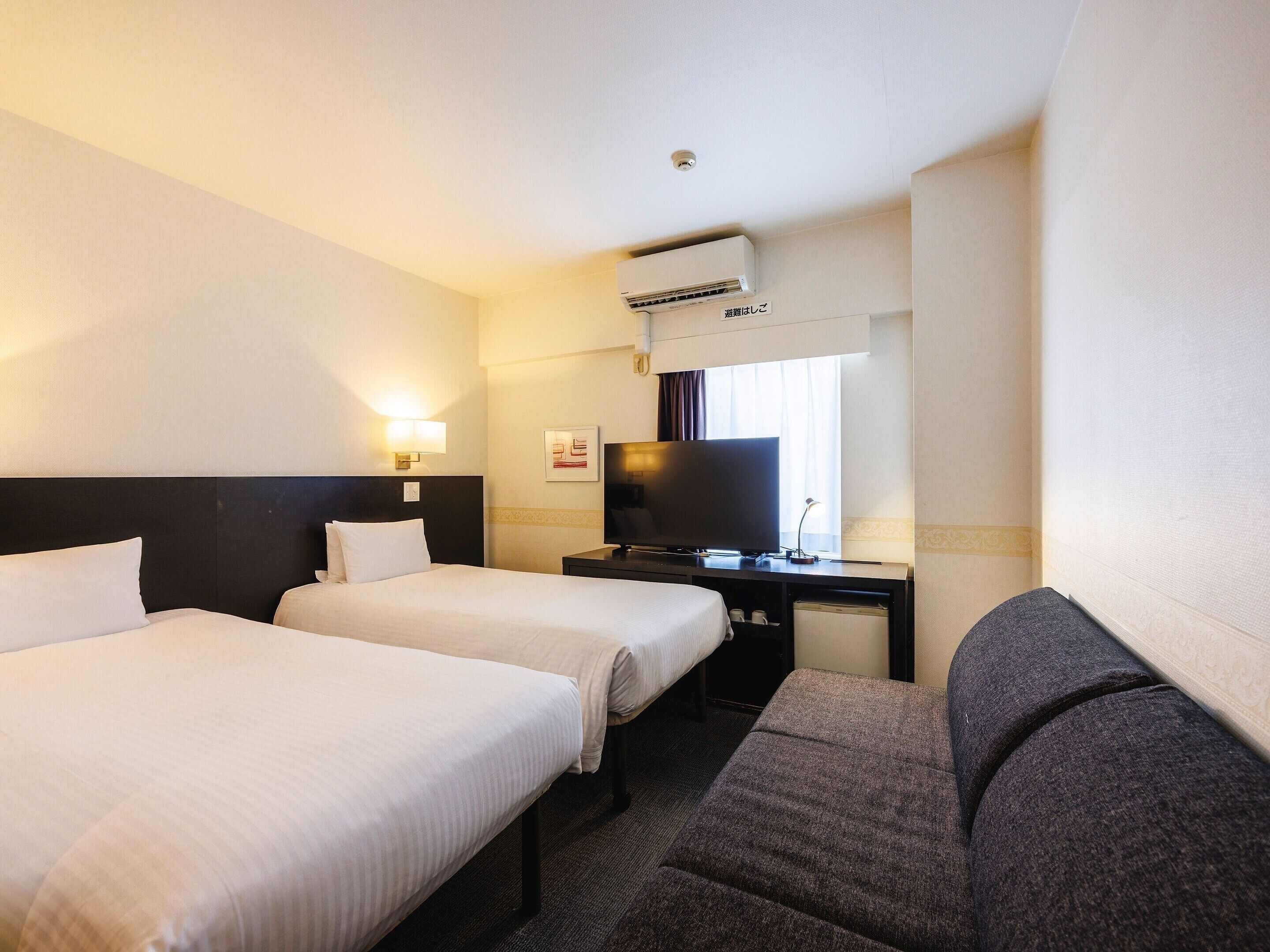 A hotel room with two beds, a desk, a television, and a window.