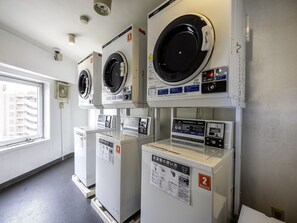 A laundry facility with multiple coin-operated washers and dryers, each labeled with usage instructions and capacity.