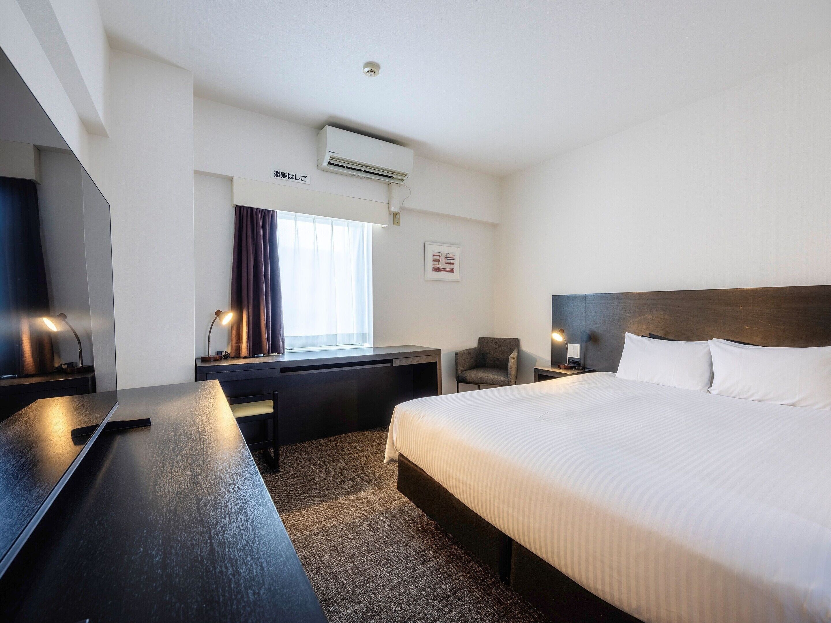 Une chambre d’hôtel équipée d’un lit, d’un bureau, d’une chaise, d’une table de chevet et d’un appareil de climatisation.
