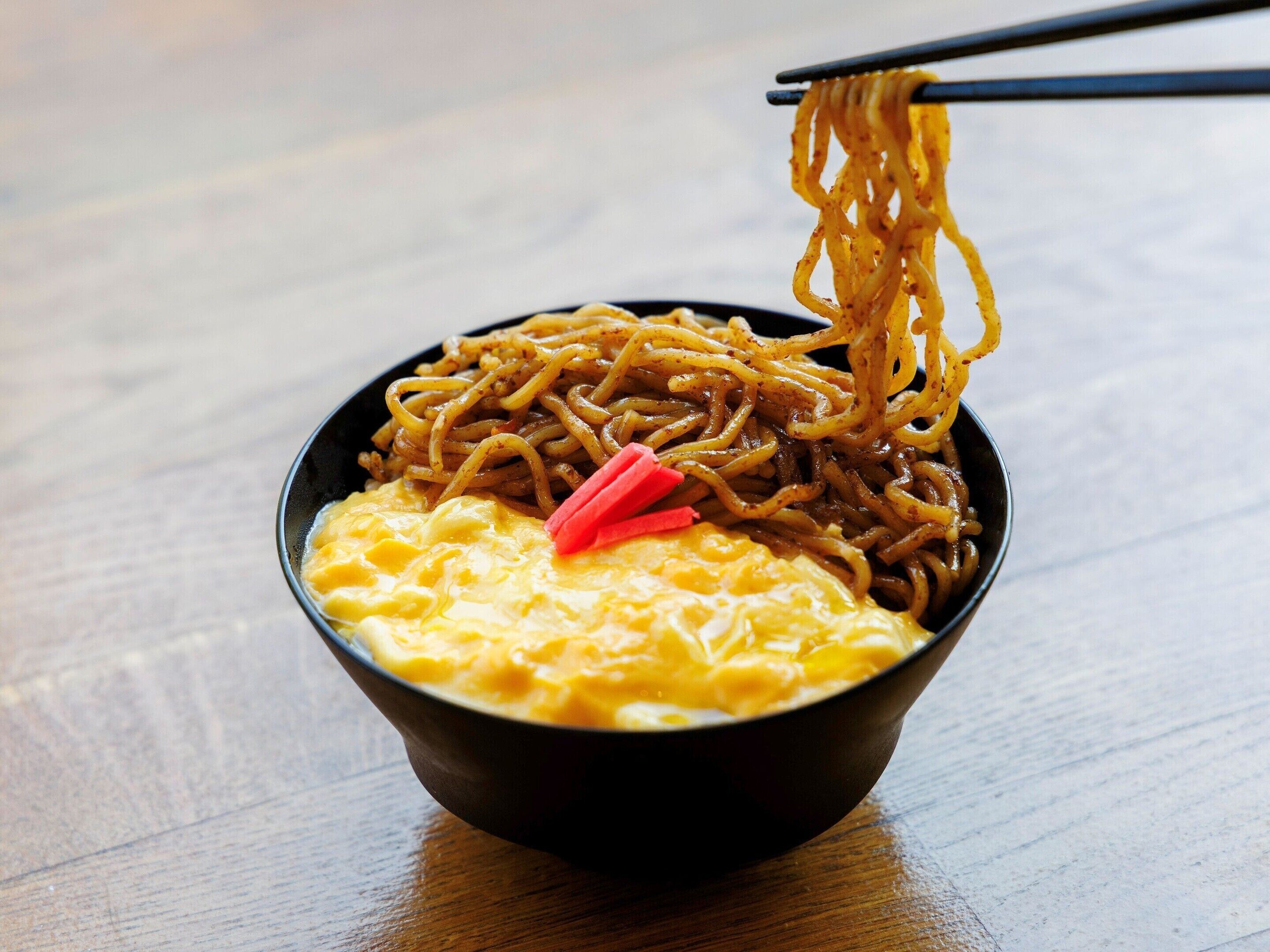 A bowl of noodles with chopsticks lifting a portion.