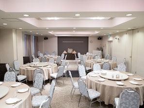 Une salle de conférence équipée de plusieurs tables rondes, chacune agrémentée d’assiettes, de verres et de couverts.
