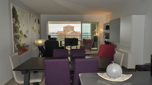 A dining area with a table and chairs, a decorative item on the table, and a view of a building through a glass door. - Vue Mer Panoramique  Confort Moderne (Les Sables-d´Olonne)