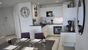 A modern kitchen with white cabinets, a black countertop, and a dining area with a table set for two. - Vue Mer Panoramique  Confort Moderne (Les Sables-d´Olonne)