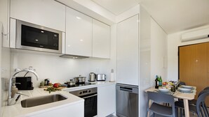 A modern kitchen with white cabinetry, stainless steel appliances, a built-in microwave, and a dining area with a table set for two. - Perfect getaway with balcony and pool (Cabanas de tavira)
