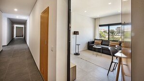 A modern hotel room with a sofa, a small table, and a lamp. There is a view of the outside through large windows. - Perfect getaway with balcony and pool (Cabanas de tavira)