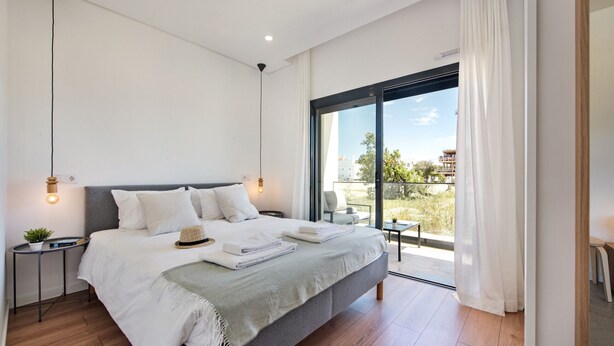 A modern bedroom with a large bed, bedside tables, a view of the outdoors, and a balcony. - Perfect getaway with balcony and pool (Cabanas de tavira)