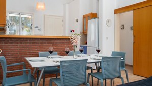 Un comedor con pared de ladrillo, una mesa blanca dispuesta con platos, vasos y cubiertos, y sillas azules.
