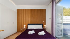 Habitación de hotel con una cama grande, pared de paneles de madera, dos lámparas de noche y vistas a una piscina a través de una puerta de vidrio.