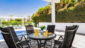 Un espacio de estar al aire libre cubierto con piscina, sillas negras y una mesa con bebidas y aperitivos.
