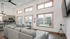 A spacious living room with a large sectional sofa, a kitchen area with a microwave and stove, and multiple windows offering views of the outdoors. - Quiet Country Oasis with Hot Tub (Hardinsburg)