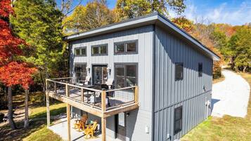 Un bâtiment à deux étages doté d’un balcon, d’un espace extérieur couvert aménagé en coin salon et d’un chemin de gravier menant à l’entrée.
