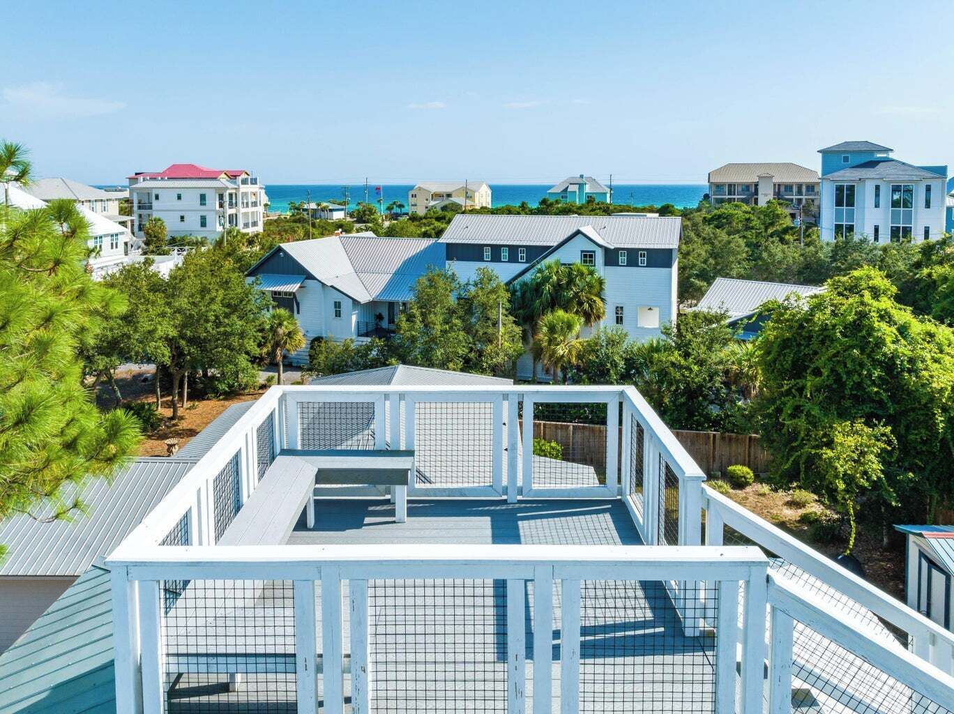 A coastal residential area with houses, a clear view of the ocean, and a fenced deck area.