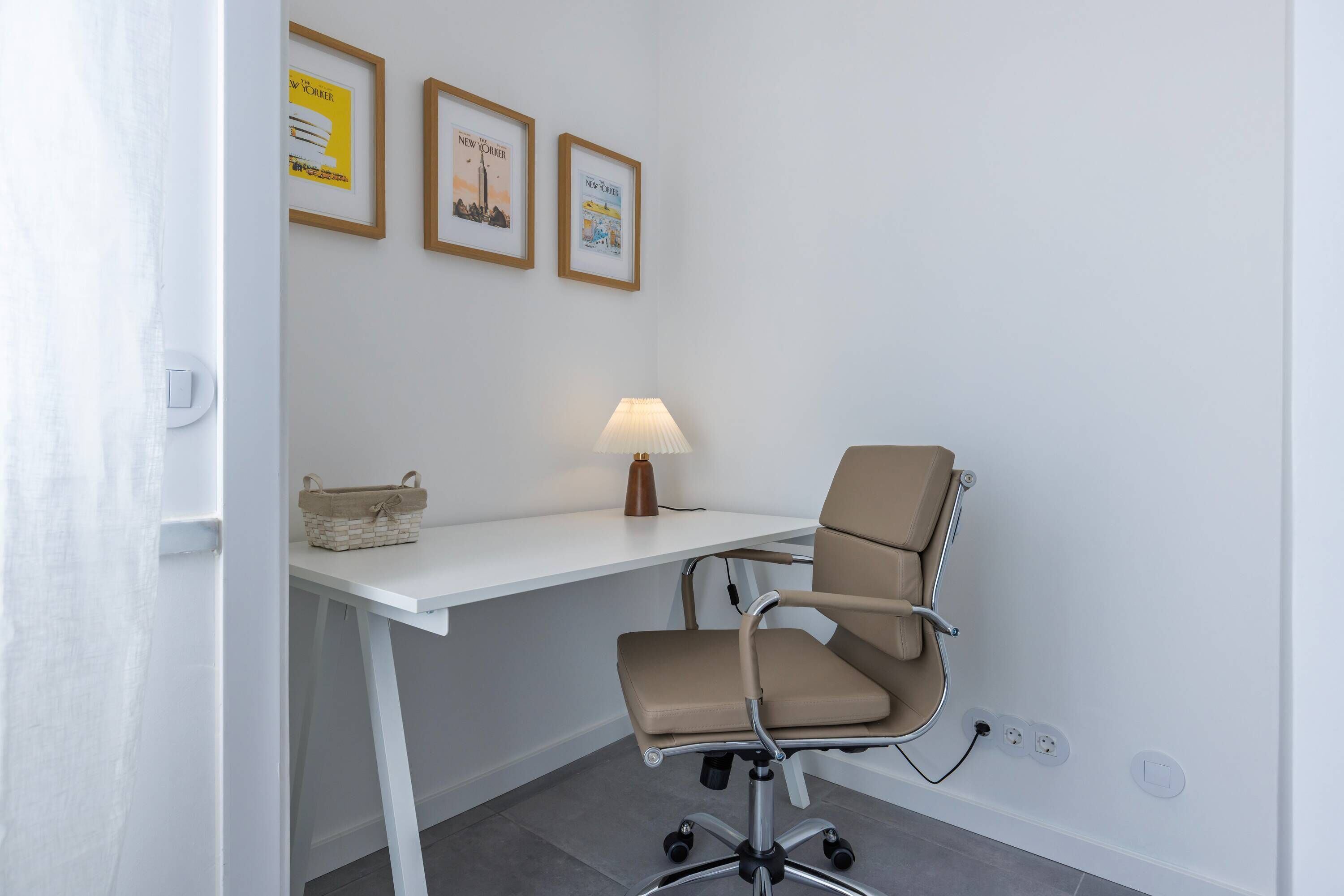 A modern office space with a white desk, a beige office chair, and a lamp. There are framed pictures on the wall.