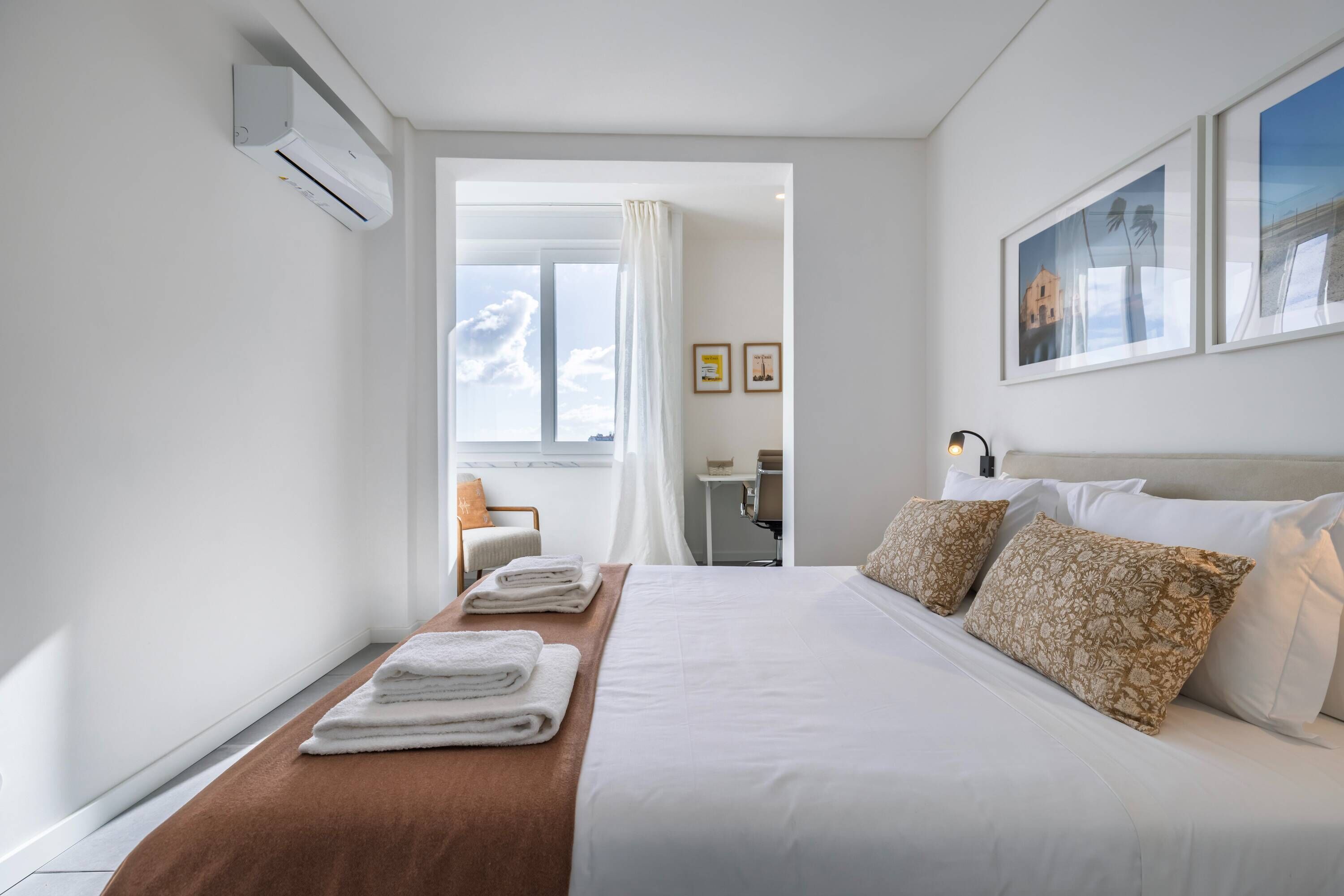 A hotel room with a neatly made bed, a window with a view, and a small table with a chair.