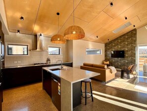 Una cocina moderna con una isla central, un rincón de comedor con sofá y una pared decorativa de piedra.