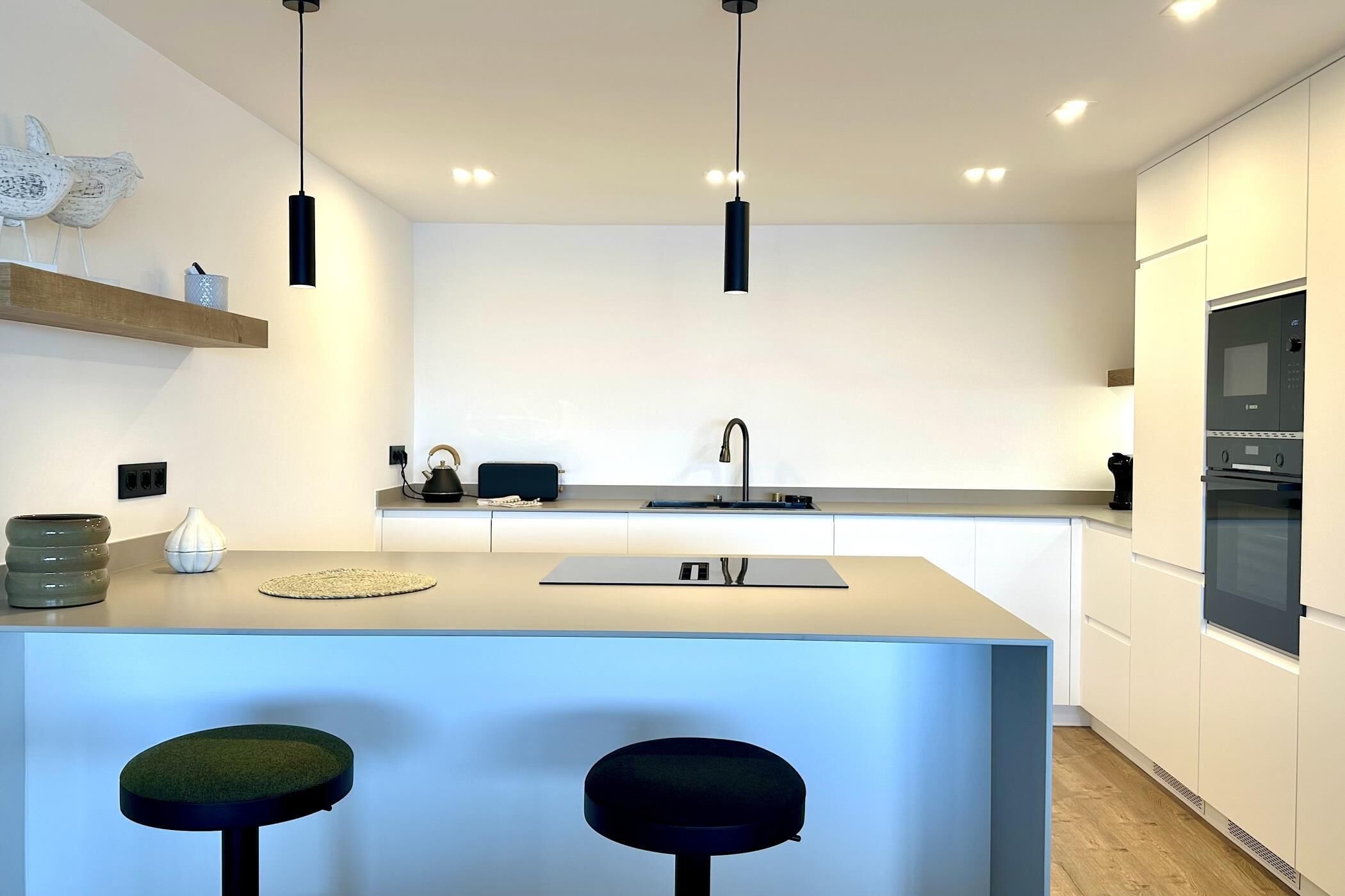 Een moderne keuken met een centraal eiland, hangende verlichting en een ingebouwde oven.