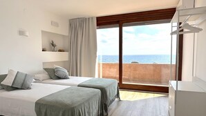 A hotel room with two beds, a large window with a view of the sea, a wardrobe, and a shelf with decorative items. - DÚPLEX FRENTE AL MAR, PISCINA PANORÁMICA, DOS PKG (Tossa de Mar)