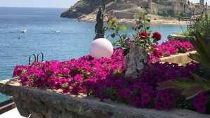 A coastal view with a stone balustrade, vibrant pink flowers, and a statue. - DÚPLEX FRENTE AL MAR, PISCINA PANORÁMICA, DOS PKG (Tossa de Mar)