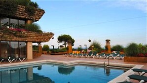 A swimming pool with lounge chairs, a stone structure with greenery, and a clear sky. - DÚPLEX FRENTE AL MAR, PISCINA PANORÁMICA, DOS PKG (Tossa de Mar)