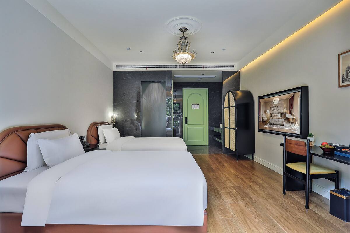 A hotel room with a large bed, a desk with a chair, a green door, and a framed picture on the wall.