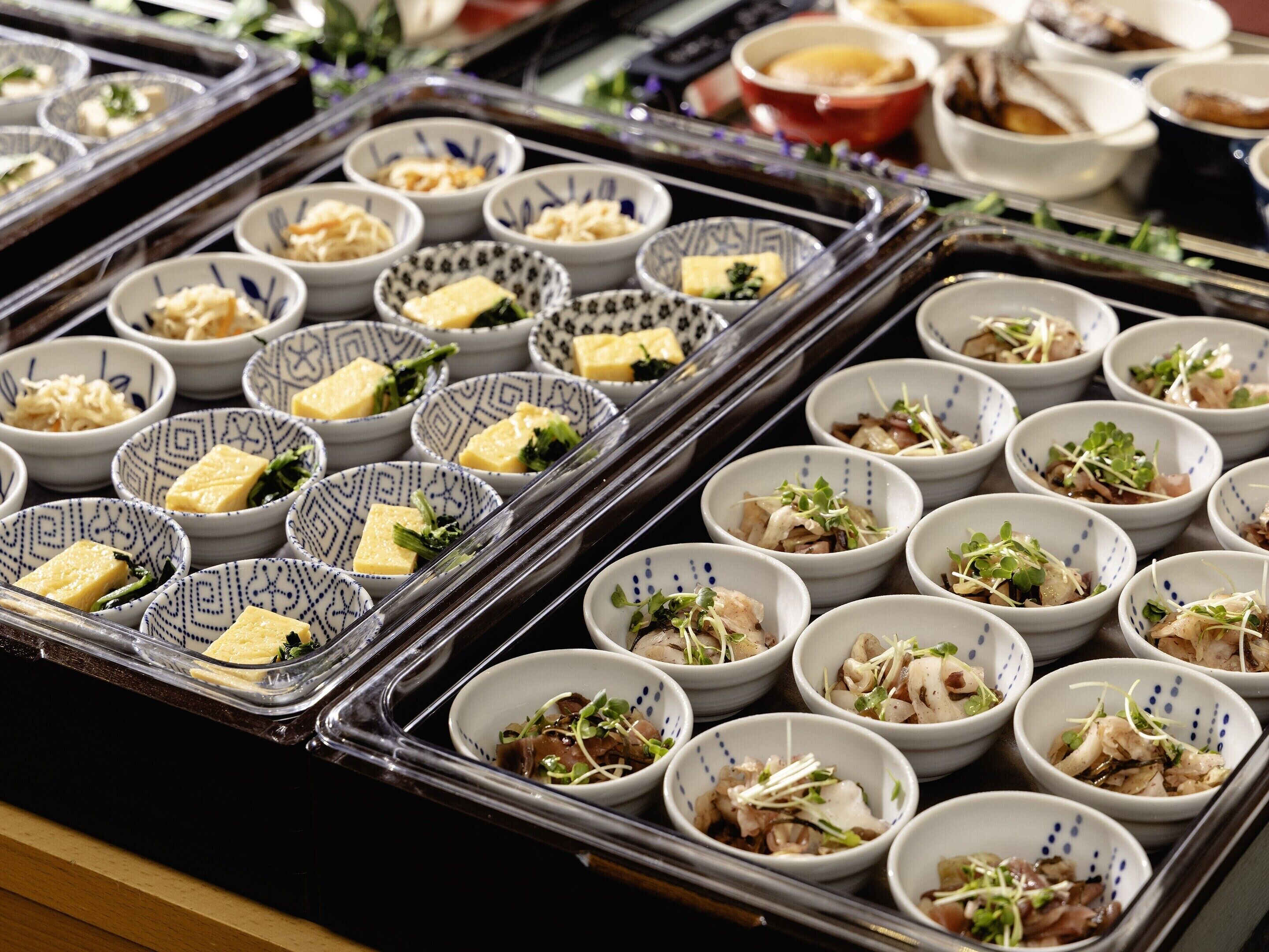 A buffet with various dishes in patterned bowls, including some with cheese and greens.