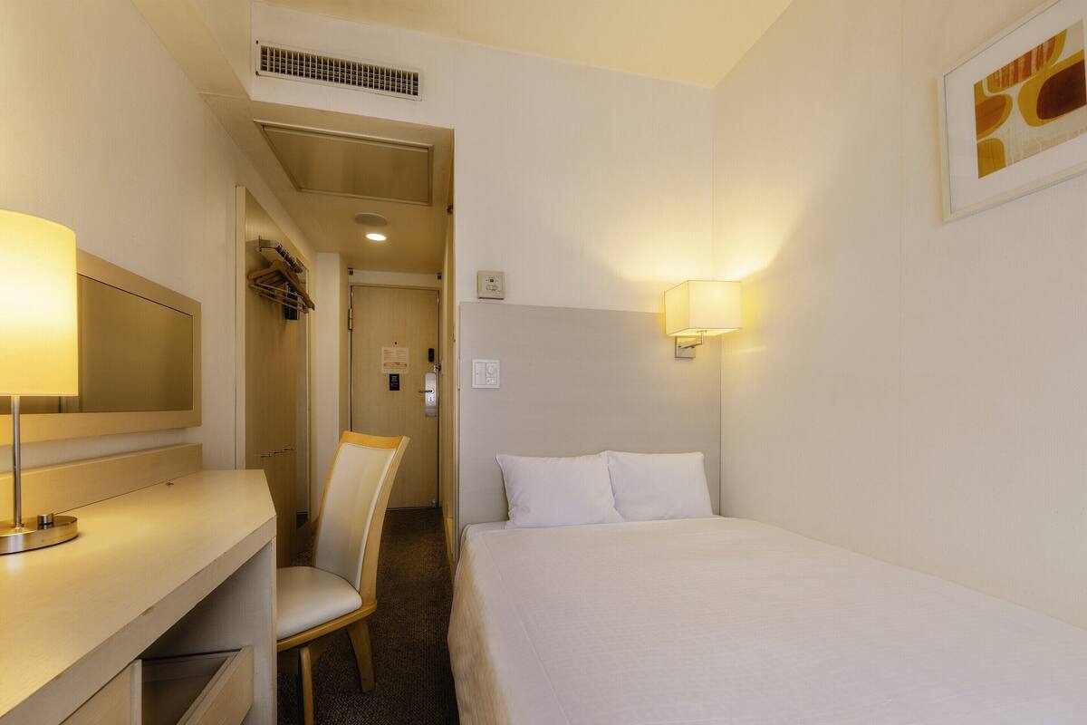 Ein Hotelzimmer mit einem Bett, einem Schreibtisch mit Lampe, einem Sessel und einer Wandleuchte.