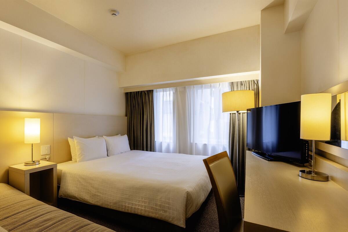 Ein Hotelzimmer mit einem großen Bett, einem kleineren Bett, einem Schreibtisch mit Fernseher und einem Sessel.