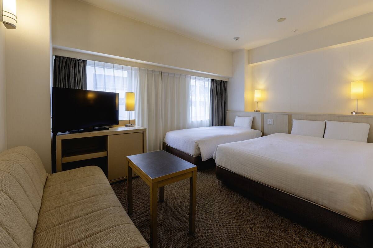 Ein Hotelzimmer mit zwei Betten, einem Fernseher, einem kleinen Tisch und einem Sofa.