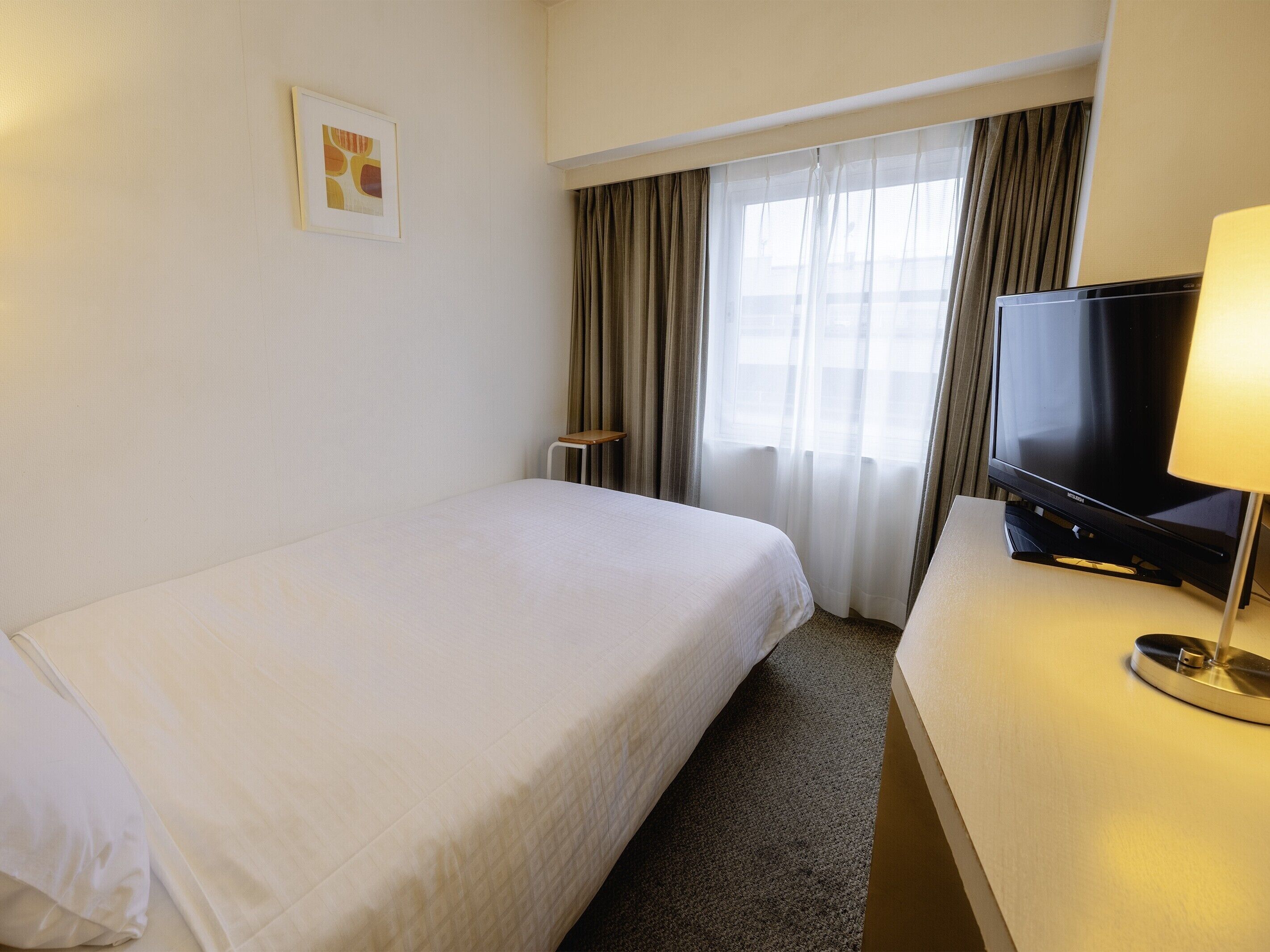 Habitación de hotel con cama, televisión en un mueble bajo, una mesita y una ventana con cortinas.