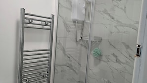 A bathroom with a glass-enclosed shower, a chrome towel rack, and a white shower control panel.