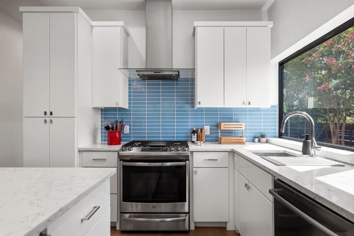 A modern kitchen with white cabinets, a stainless steel stove, and a blue-tiled backsplash.
