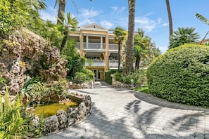 Un hotel con un vialetto lastricato, un giardino roccioso e un siepe ben curata.