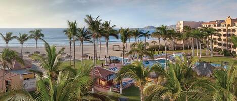 A resort with a pool area, palm trees, and a beach view.