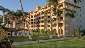 Un hôtel à plusieurs étages doté de balcons, de palmiers et d’une pelouse bien entretenue.