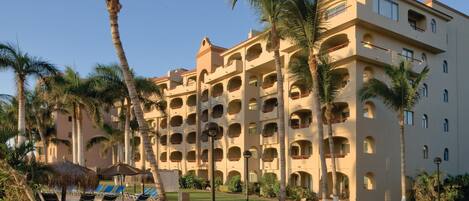 A multi-story hotel with balconies, palm trees, and a well-maintained lawn.