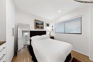 Une chambre d’hôtel comprenant un lit, une armoire, un miroir, une fenêtre avec des stores et des œuvres d’art accrochées au mur.