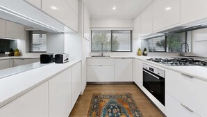 A modern kitchen with white cabinetry, a gas stove, an oven, and a window with blinds.