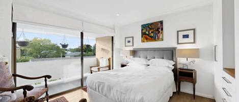 Une chambre d’hôtel avec un grand lit, un bureau, une chaise, une fenêtre donnant sur un beau paysage et des œuvres d’art accrochées au mur.