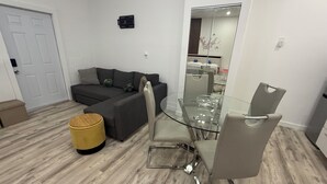 A modern living room with a glass dining table, grey sofa, and a yellow ottoman.