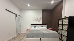 A modern bedroom with a large bed, a wardrobe, a nightstand, and a decorative wall piece.