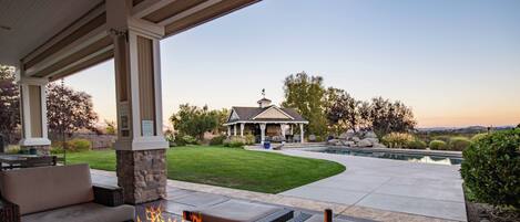An outdoor patio with a fire feature, seating, and a view of a gazebo and pool.