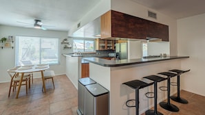 Una cocina moderna con una isla central, taburetes de bar y un comedor con mesa y sillas.