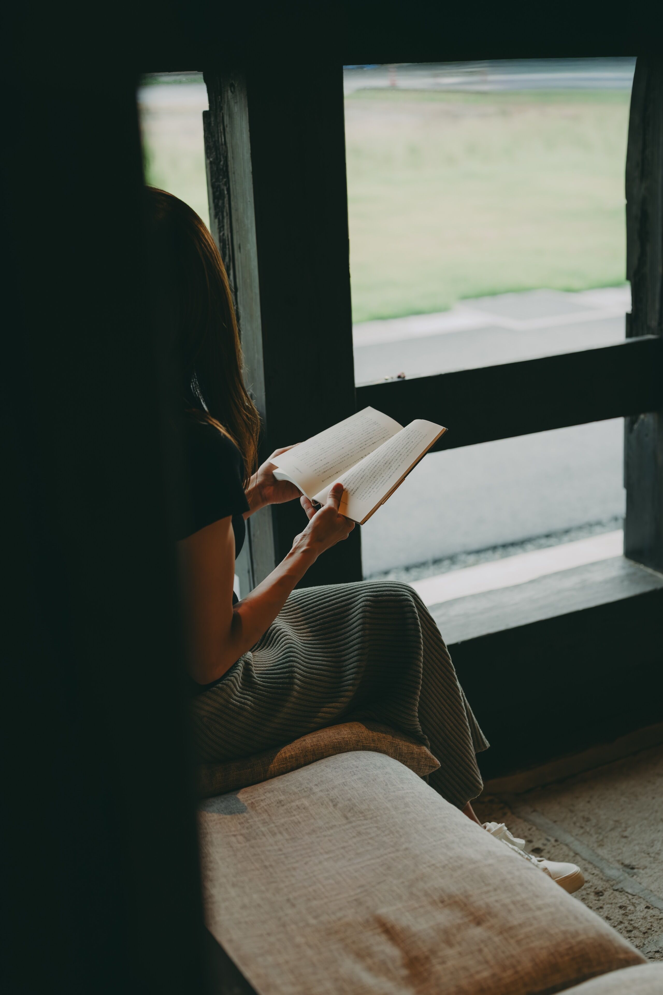 Una persona sentada junto a una ventana, leyendo un libro.