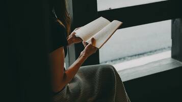 Una persona sentada junto a una ventana, leyendo un libro.