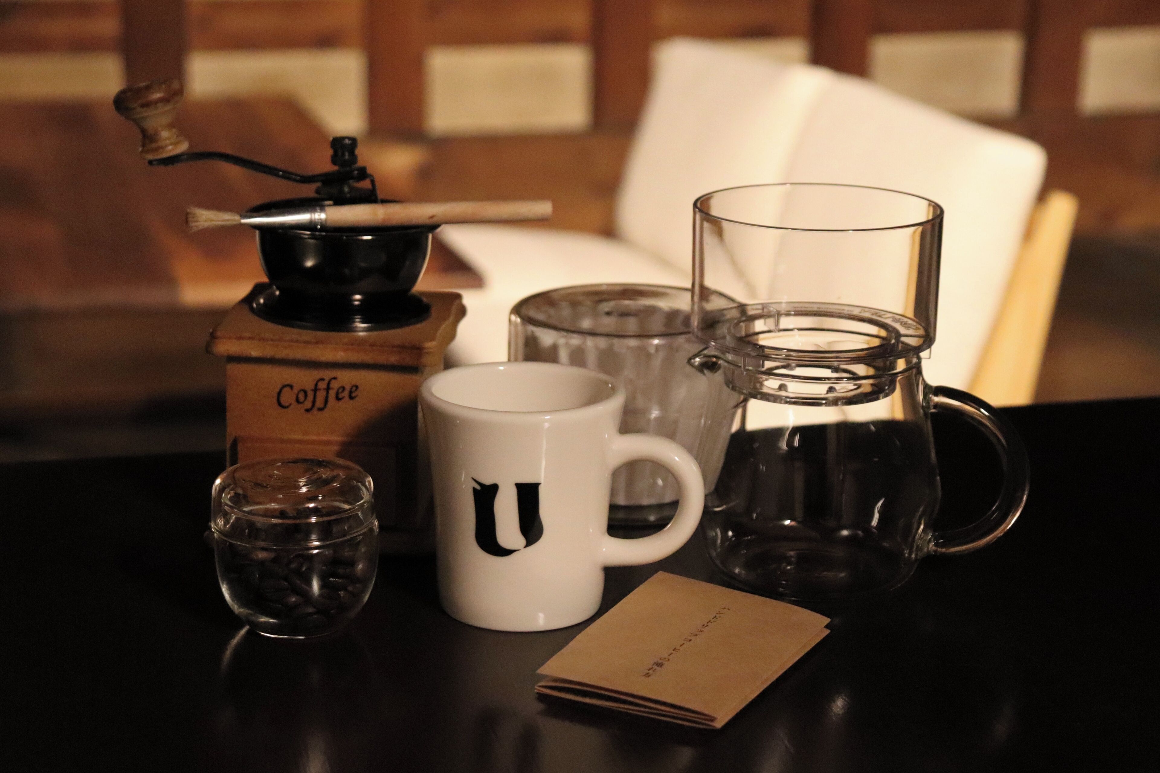A coffee maker, a white mug with a letter, a glass pitcher, a glass cup, and a small glass container on a table.