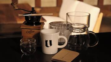 A coffee maker, a white mug with a letter, a glass pitcher, a glass cup, and a small glass container on a table.